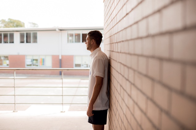 Side profile of person in Summer clothing leaning against brick wall of school exterior