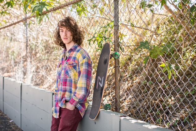 Young skateboarder leaning against a fence